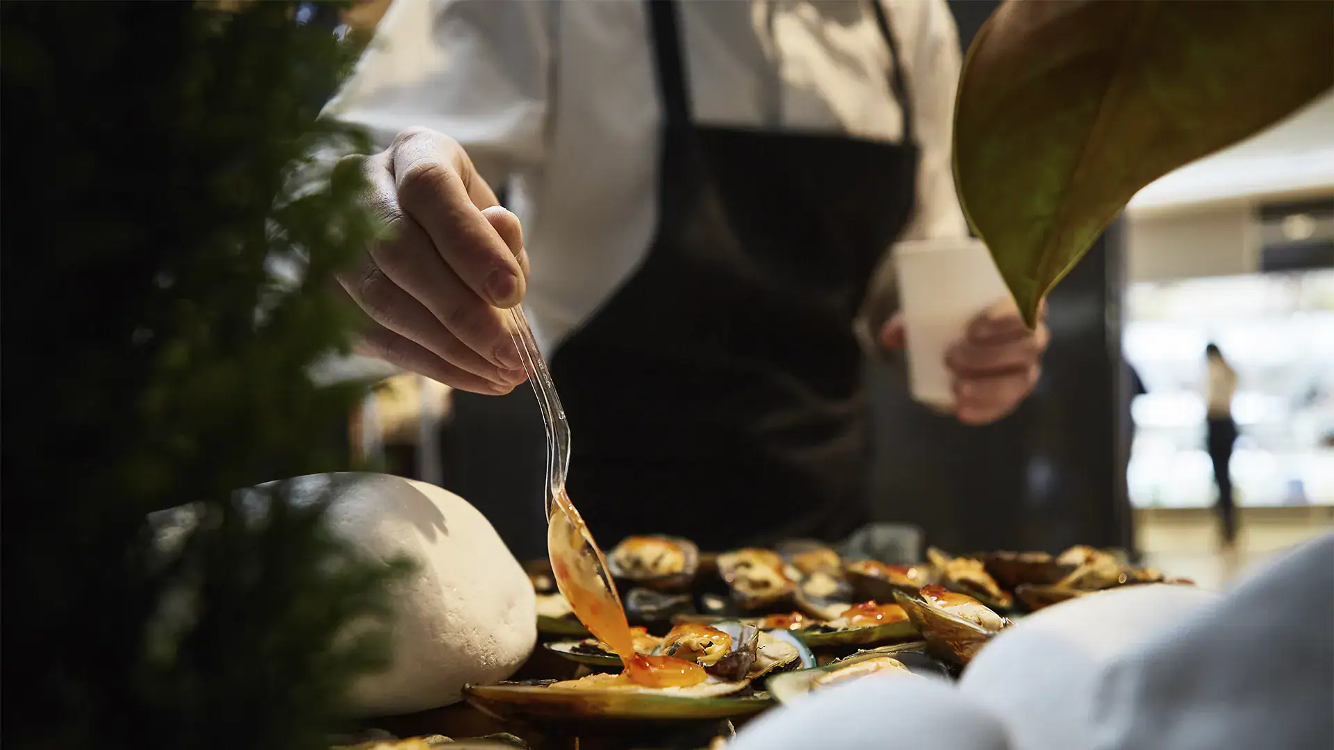 A delicious seafood dish being prepared outdoors in Opulencia, Nosara, Costa Rica, showcasing fresh oysters and a chef adding sauce, with a relaxed tropical atmosphere.